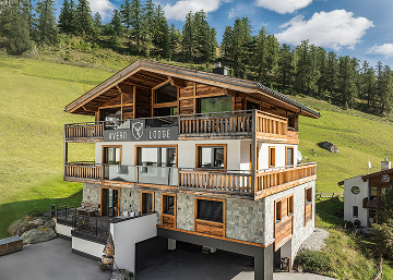 Ein modernes Holzchalet, unterkunft Samnaun, mit Balkonen an einem grasbewachsenen Hang.