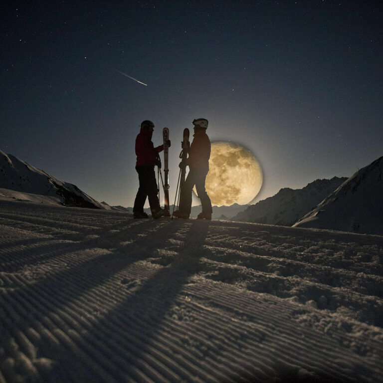 Zwei Skifahrer geniessen einen Skiurlaub in Samnaun bei Vollmond auf verschneiten Pisten.