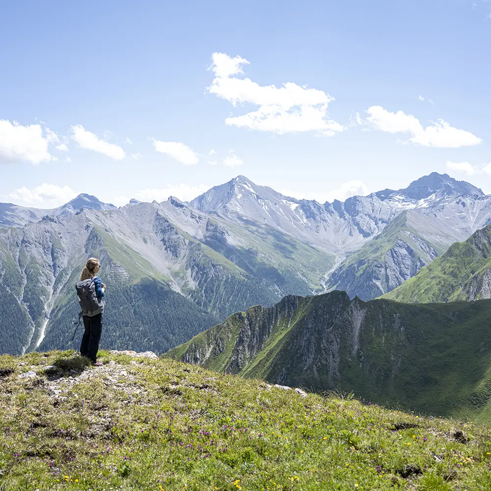 Person Trailrunning Samnaun Hügel, mit Blick auf schroffe Berge unter einem klaren blauen Himmel.