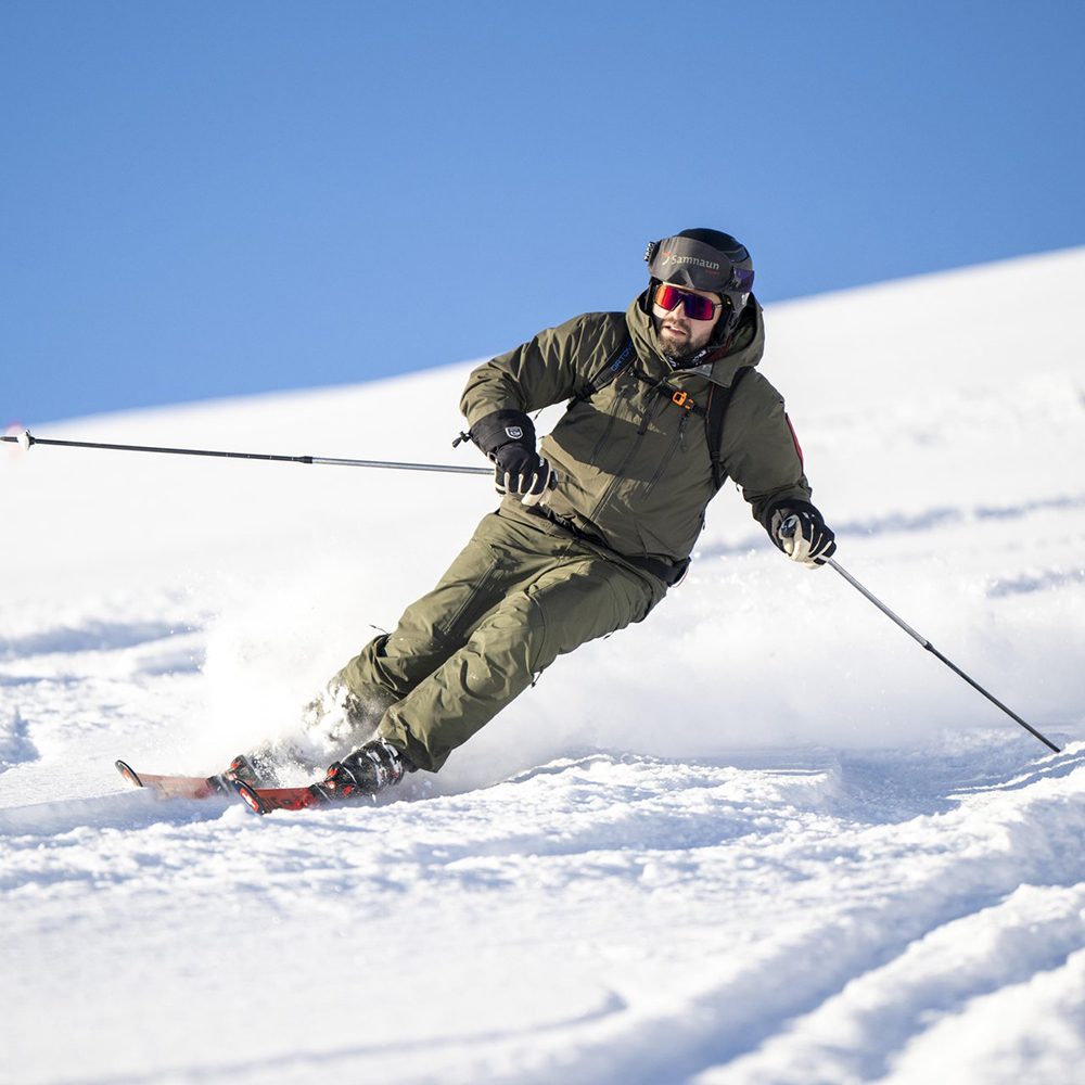 Person beim Skifahren im hellen Sonnenlicht auf einem Skiurlaub in Samnaun, mit grüner Ausrüstung und Helm.