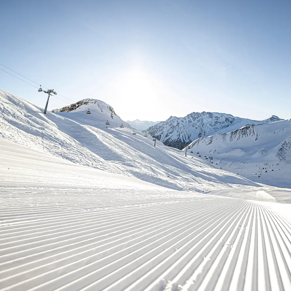 Frisch präparierte Samnauner Skipiste mit Sesselliften und verschneiten Bergen unter strahlend blauem Himmel.