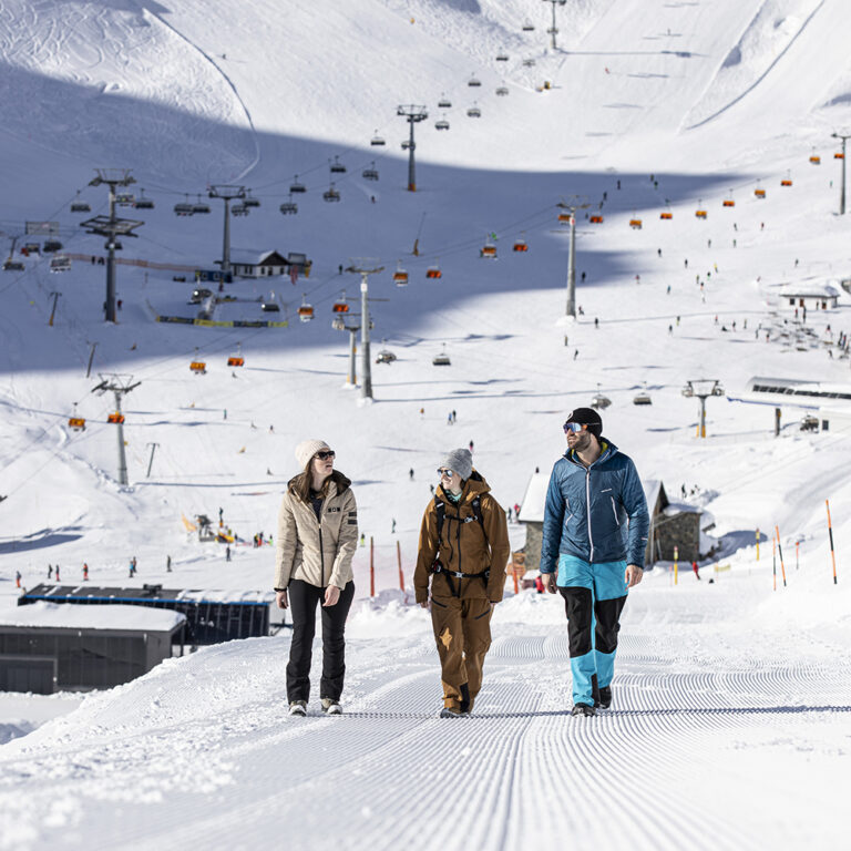 Drei Personen gehen auf einer verschneiten Skipiste während ihres Skiurlaubs in Samnaun.