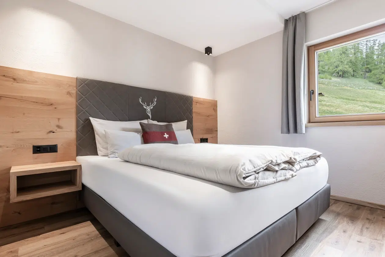 Modernes Schlafzimmer in der Ferienwohnung Samnaun mit einem Doppelbett, Holzakzenten und Blick ins Grüne.