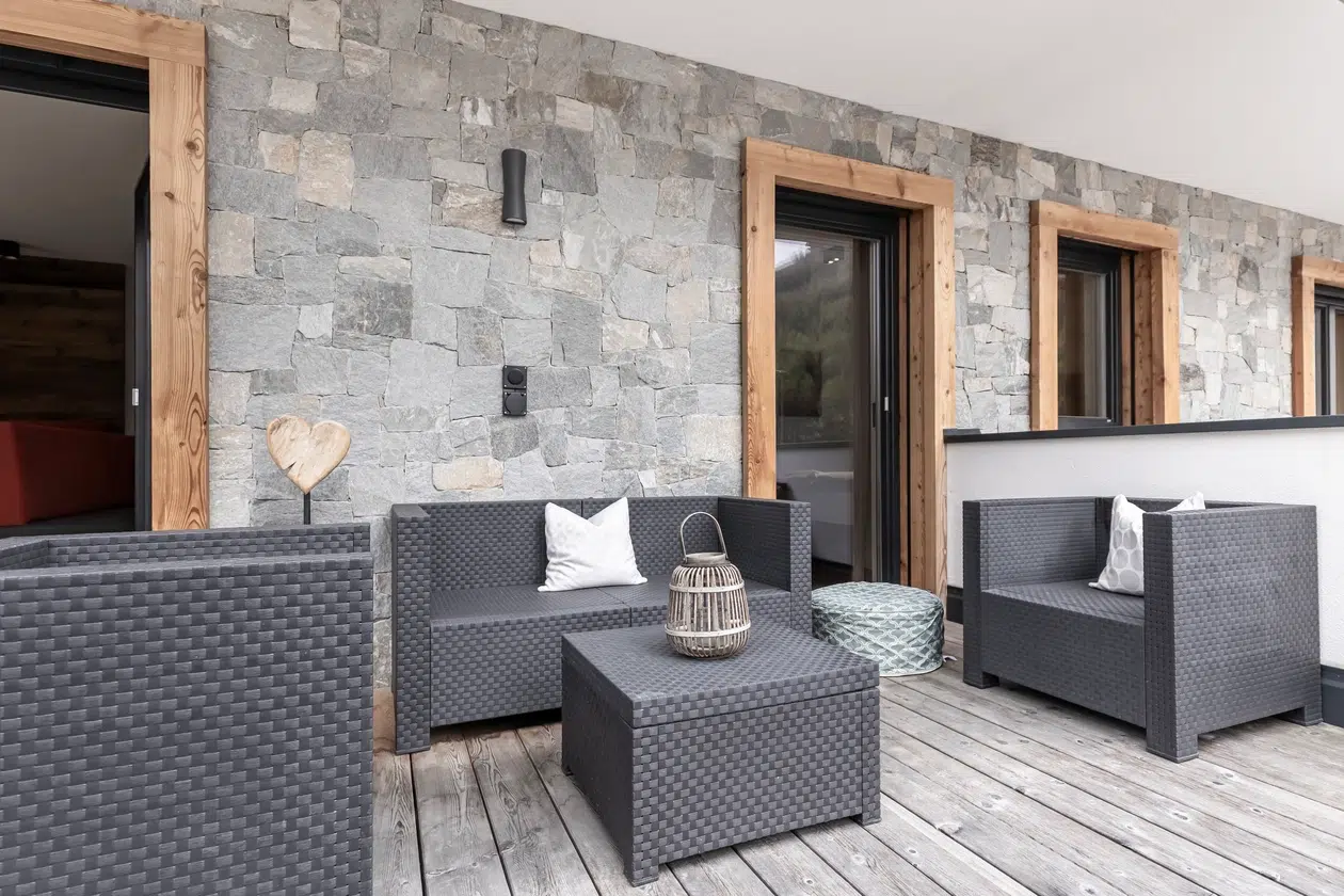 Moderner Innenhof der Ferienwohnung Samnaun mit grauen Korbmöbeln und holzgerahmten Fenstern.