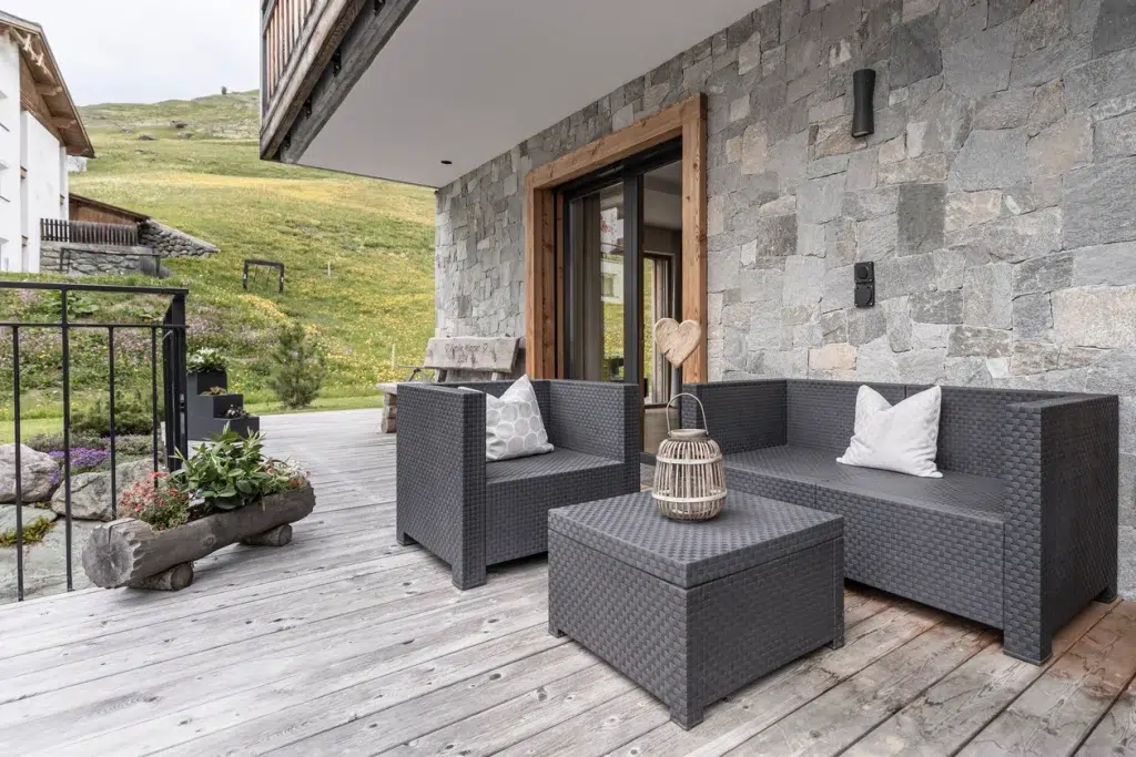 Moderner Innenhof der Ferienwohnung Samnaun mit grauen Korbmöbeln auf einer Holzterrasse.