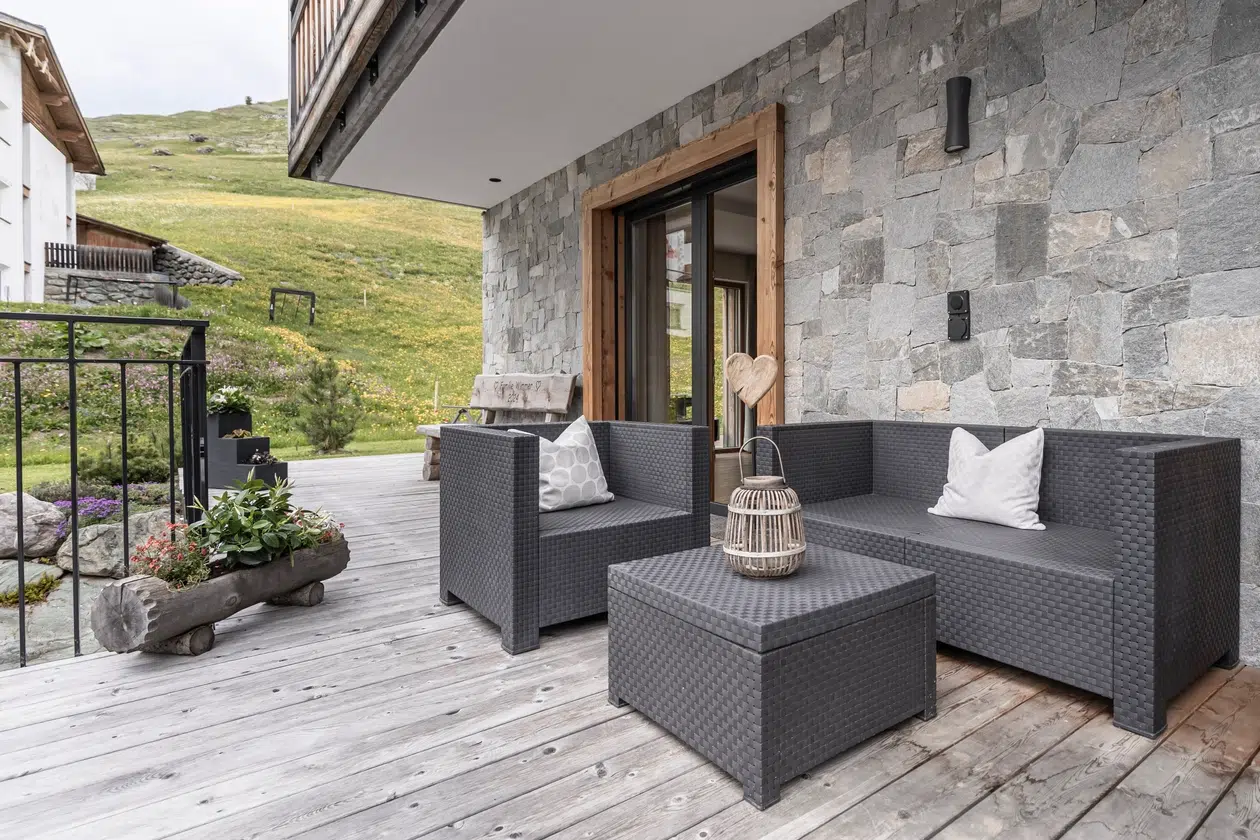 Moderner Innenhof der Ferienwohnung Samnaun mit grauen Korbmöbeln auf einer Holzterrasse.