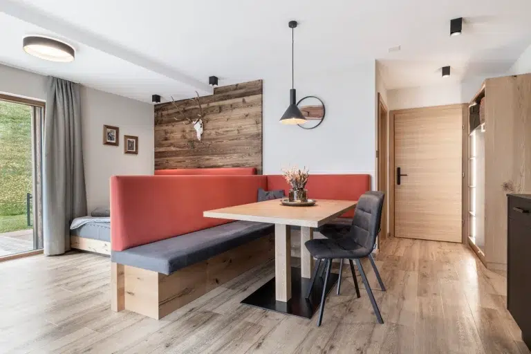 Moderne Essecke im Ferienhaus Samnaun mit Holztisch, roter Bank und schwarzen Stühlen.