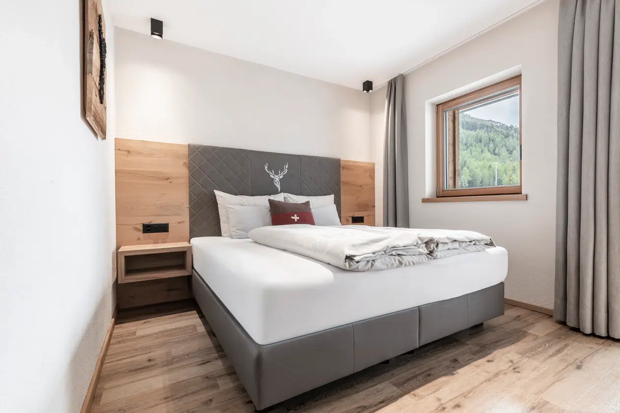 Modernes Schlafzimmer in der Ferienwohnung Samnaun mit großem Bett, Holzakzenten und Blick ins Grüne.