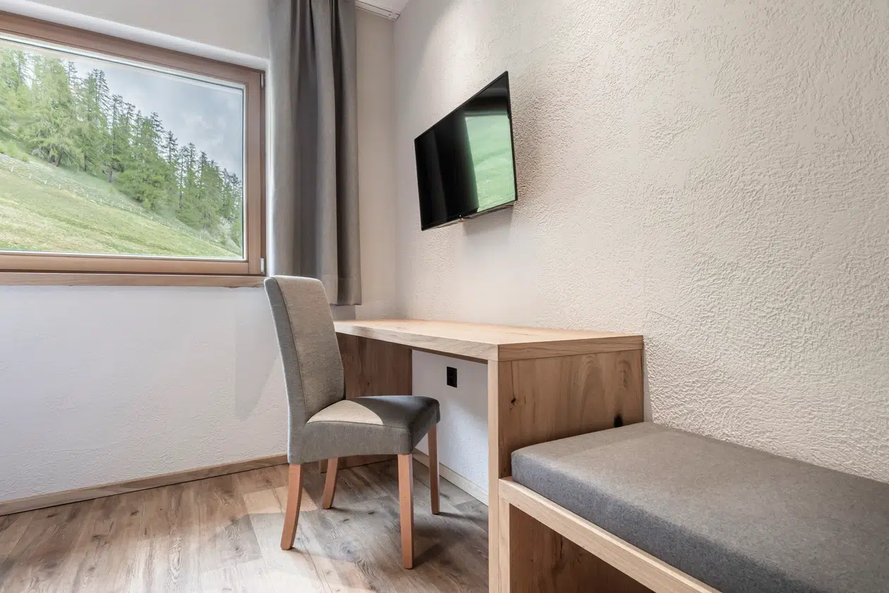 Minimalistisches Zimmer mit Schreibtisch, Stuhl, TV, Fenster und Waldblick in der Ferienwohnung Samnaun.