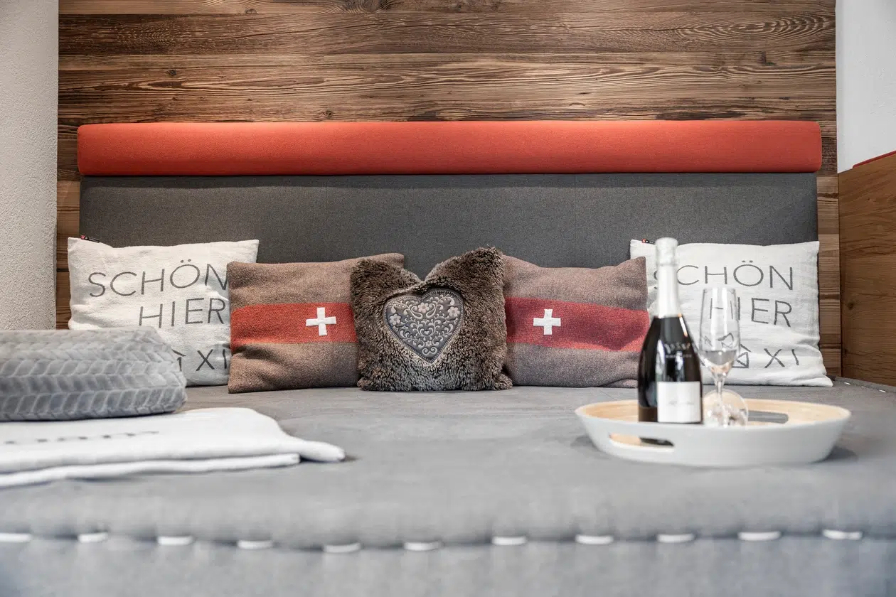Gemütliches Bett mit Schweizer Kissen, Wein und Gläsern in einer stilvollen Ferienwohnung Samnaun.