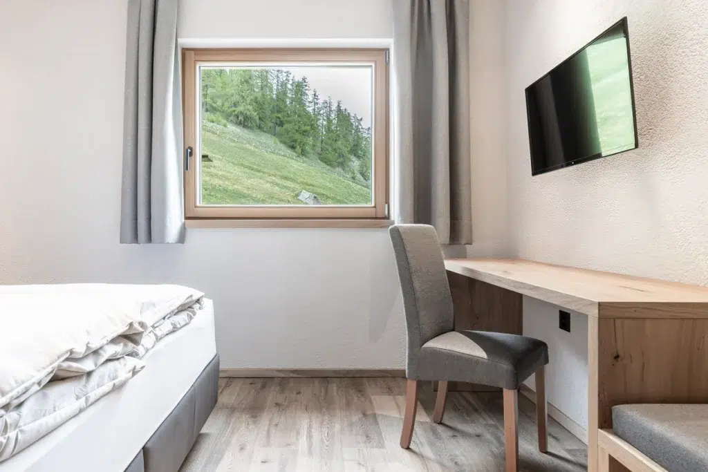 Minimalistisches Schlafzimmer im Ferienhaus Samnaun mit Schreibtisch, Stuhl, TV und Blick auf die Berge.
