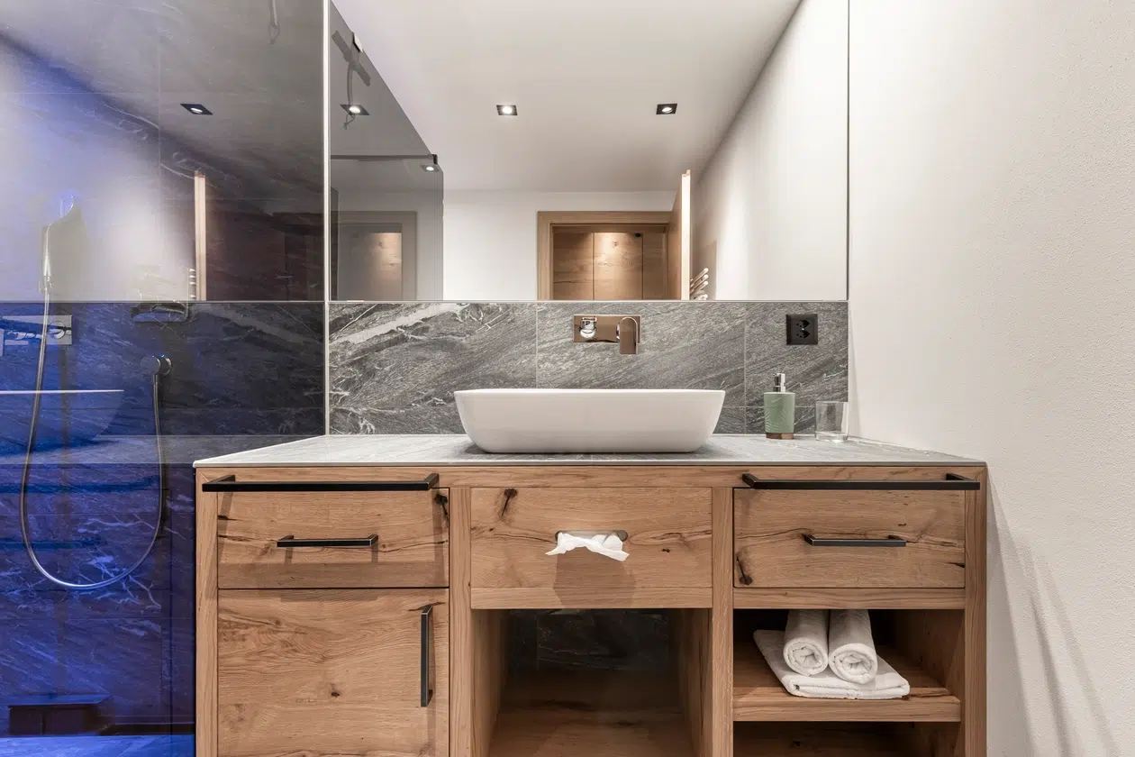 Modernes Badezimmer in der Ferienwohnung Samnaun mit hölzernem Waschtisch, Gefäßwaschbecken und Glasdusche.