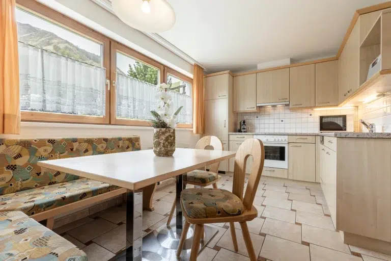 Helle Küche in der Ferienwohnung Samnaun mit Holzschränken, Esstisch, Stühlen und Bank.
