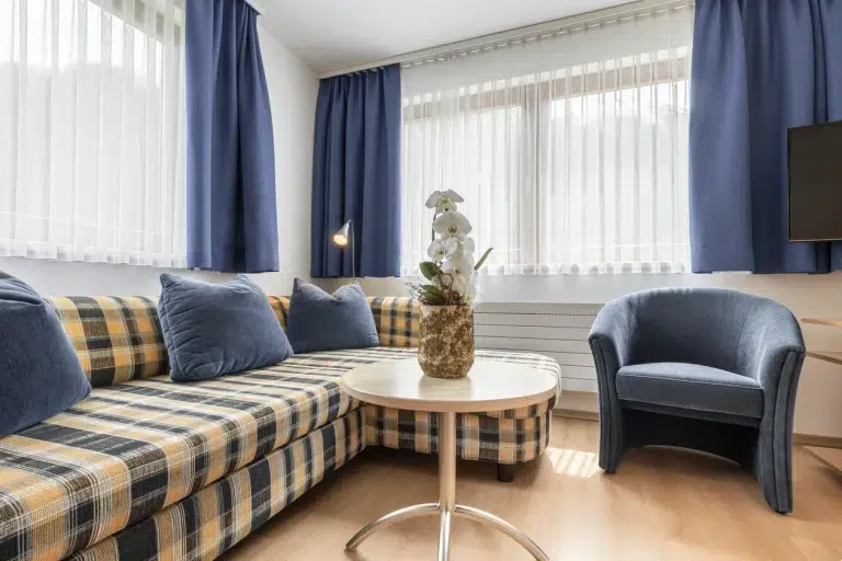 Gemütliches Wohnzimmer in der Ferienwohnung Samnaun mit kariertem Sofa, blauem Sessel und getöpferter Orchidee.