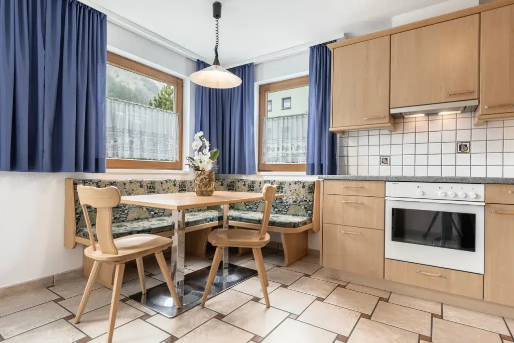 Gemütliche Küche mit Holzschränken, Ferienwohnung Samnaun-Ecke und blauen Vorhängen an den Fenstern.