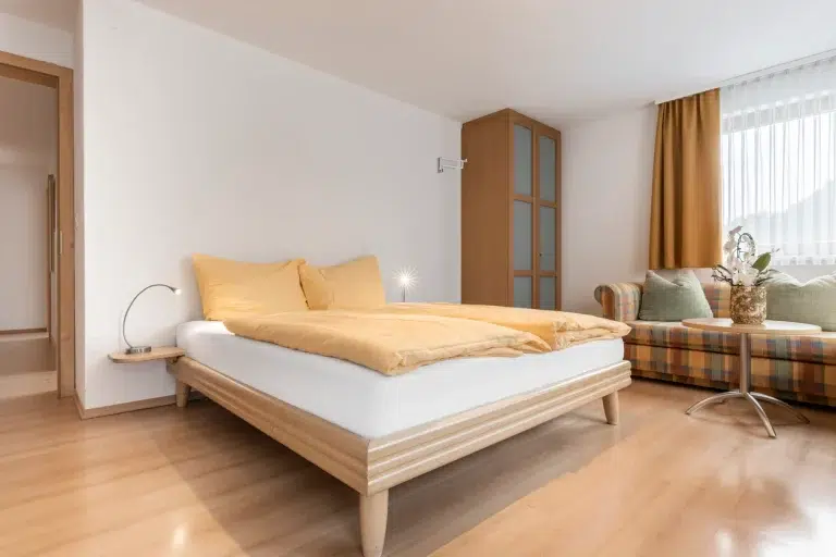 Modernes Schlafzimmer in den Ferienwohnungen Samnaun mit einem Doppelbett, gelber Bettwäsche und einem Sofa.