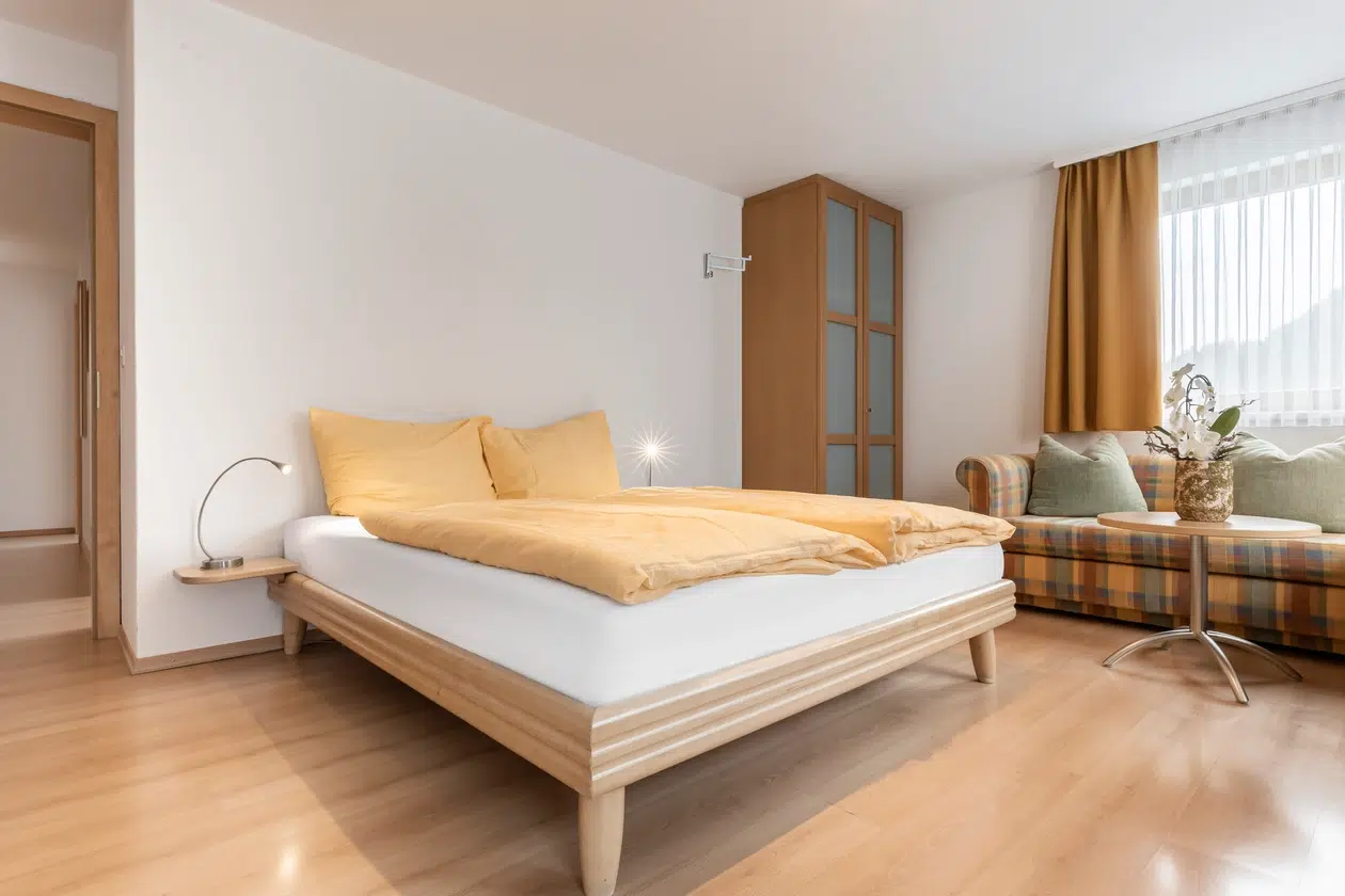 Modernes Schlafzimmer in den Ferienwohnungen Samnaun mit einem Doppelbett, gelber Bettwäsche und einem Sofa.