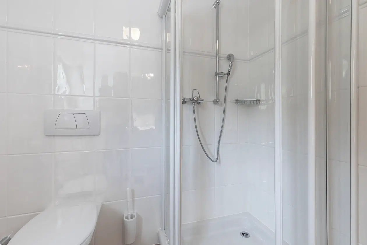 Modernes, weißes Badezimmer in der Ferienwohnung Samnaun mit Dusche, Glastür und wandmontierten Spülknöpfen.