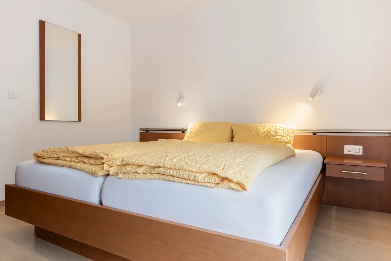 Modernes Schlafzimmer in der Ferienwohnung Samnaun mit einem Holzbett, gelber Bettwäsche und Wandleuchten.