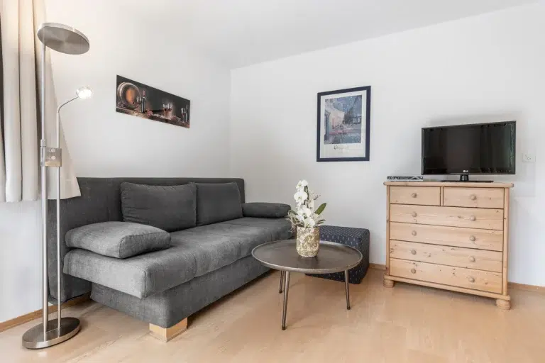 Ein gemütliches Wohnzimmer in den Ferienwohnungen Samnaun mit einem grauen Sofa, einem runden Tisch und Wandkunst.