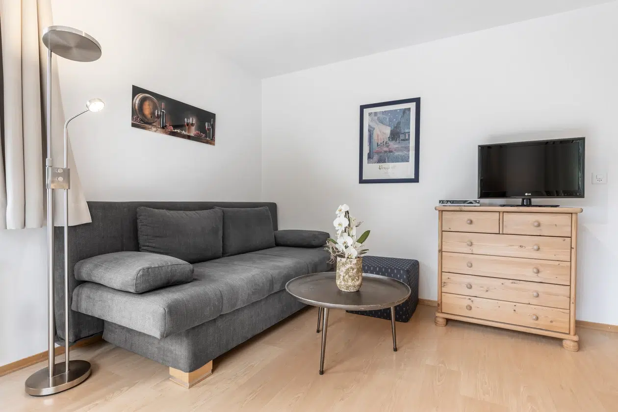 Ein gemütliches Wohnzimmer in den Ferienwohnungen Samnaun mit einem grauen Sofa, einem runden Tisch und Wandkunst.