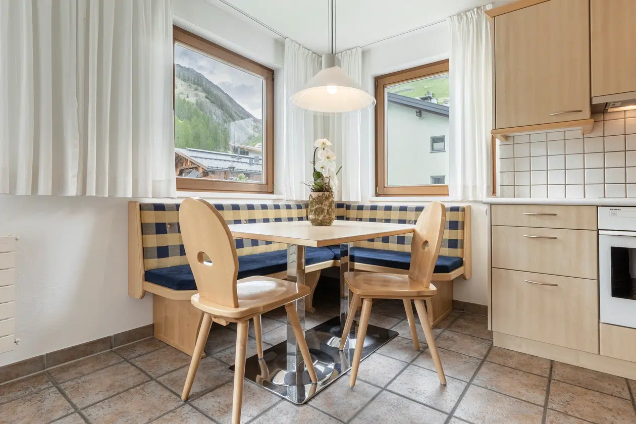 Gemütliche Küchenecke mit Holzmöbeln, blau karierter Bank und Bergblick in der Ferienwohnung Samnaun.