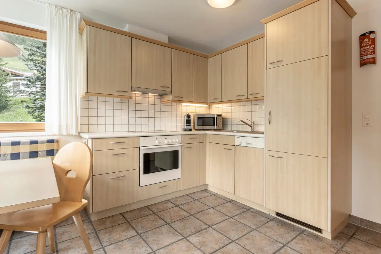 Moderne Küche in der Ferienwohnung Samnaun mit hellen Holzschränken und großem Fenster mit Blick nach draußen.