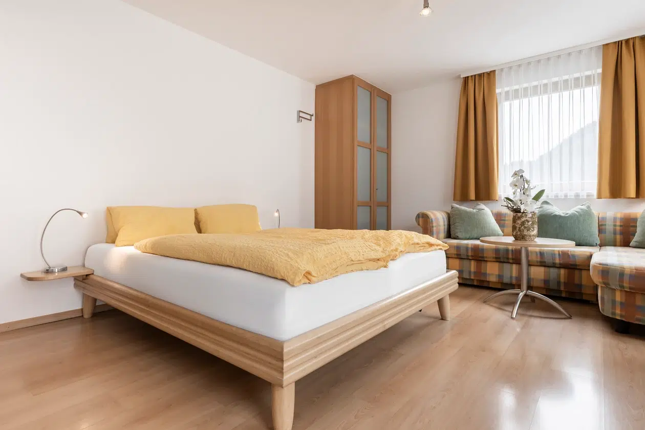Helles Schlafzimmer in der Ferienwohnung Samnaun mit Doppelbett, gelbem Bettzeug, Sofa und Kleiderschrank.