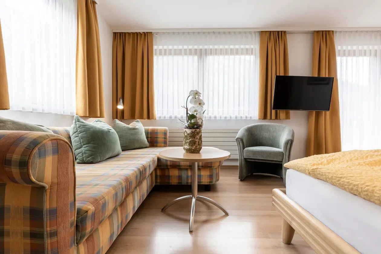 Helles Hotelzimmer in der Ferienwohnung Samnaun mit kariertem Sofa, grünem Sessel und gelben Vorhängen.