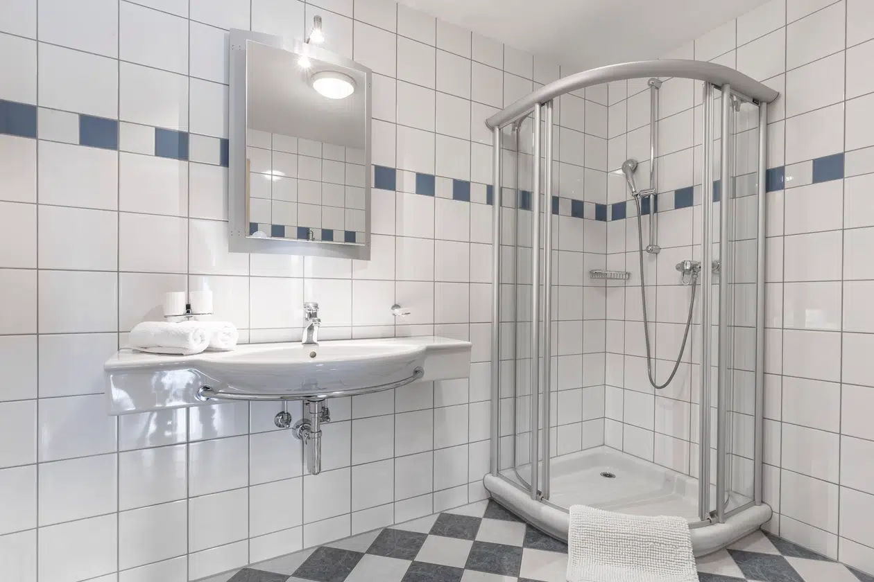 Modernes Badezimmer in der Ferienwohnung Samnaun mit Glasdusche, Wandwaschbecken, Spiegel, geflieste Wände.