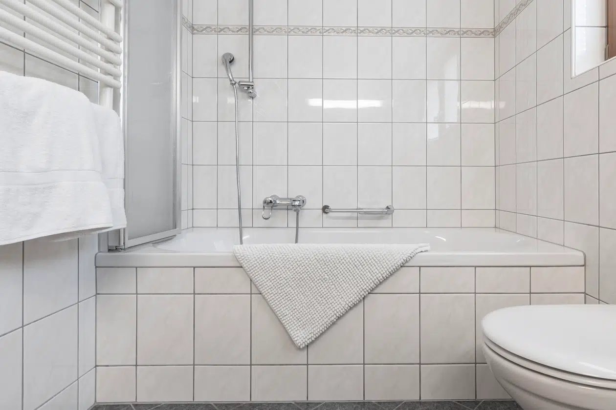 Weiß gefliestes Badezimmer in der Ferienwohnung Samnaun mit Badewanne, Dusche und Handtuch am Wannenrand.