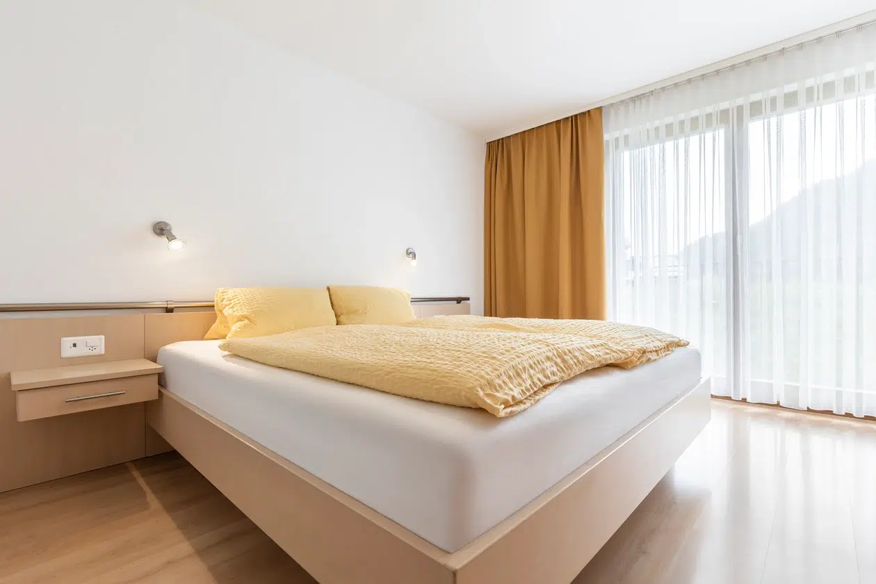 Minimalistisches Schlafzimmer in der Ferienwohnung Samnaun mit gelbem Bettzeug, Holzboden, grossem Fenster.