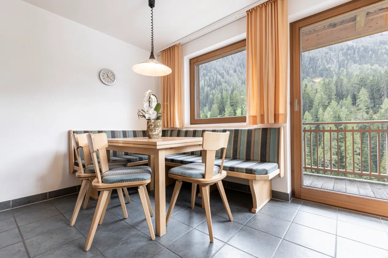 Helle Essecke mit Holzmöbeln, grossen Fenstern und Waldblick in der Ferienwohnung Samnaun.