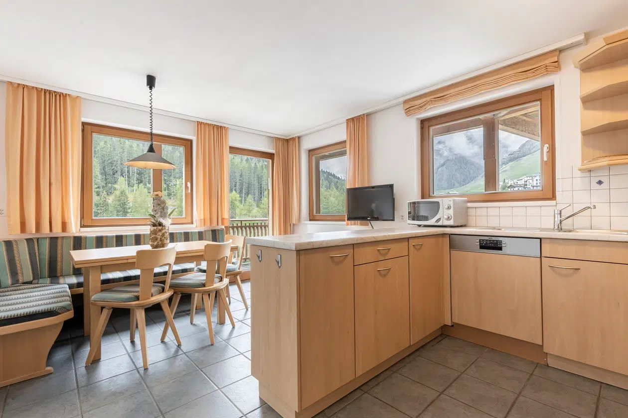 Helle Küche und Essbereich in der Ferienwohnung Samnaun mit Holzschränken und Bergblick.