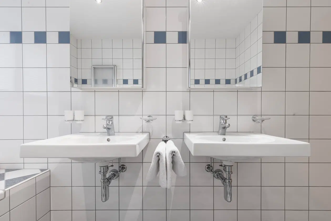 Zwei weiße Waschbecken mit Spiegeln darüber im gefliesten Badezimmer der Ferienwohnung Samnaun.