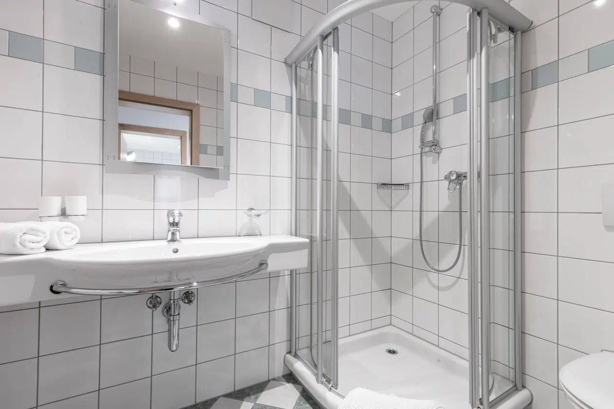 Weiß gefliestes Badezimmer in der Ferienwohnung Samnaun mit Glasdusche, Waschbecken, Spiegel und frischen Handtüchern.