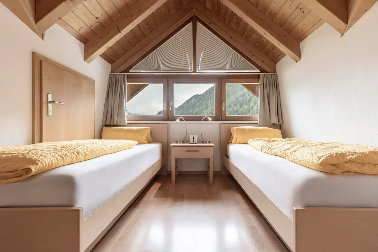 Gemütliches Dachstockzimmer in der Ferienwohnung Samnaun mit zwei Einzelbetten und Holzbalken an der Decke.