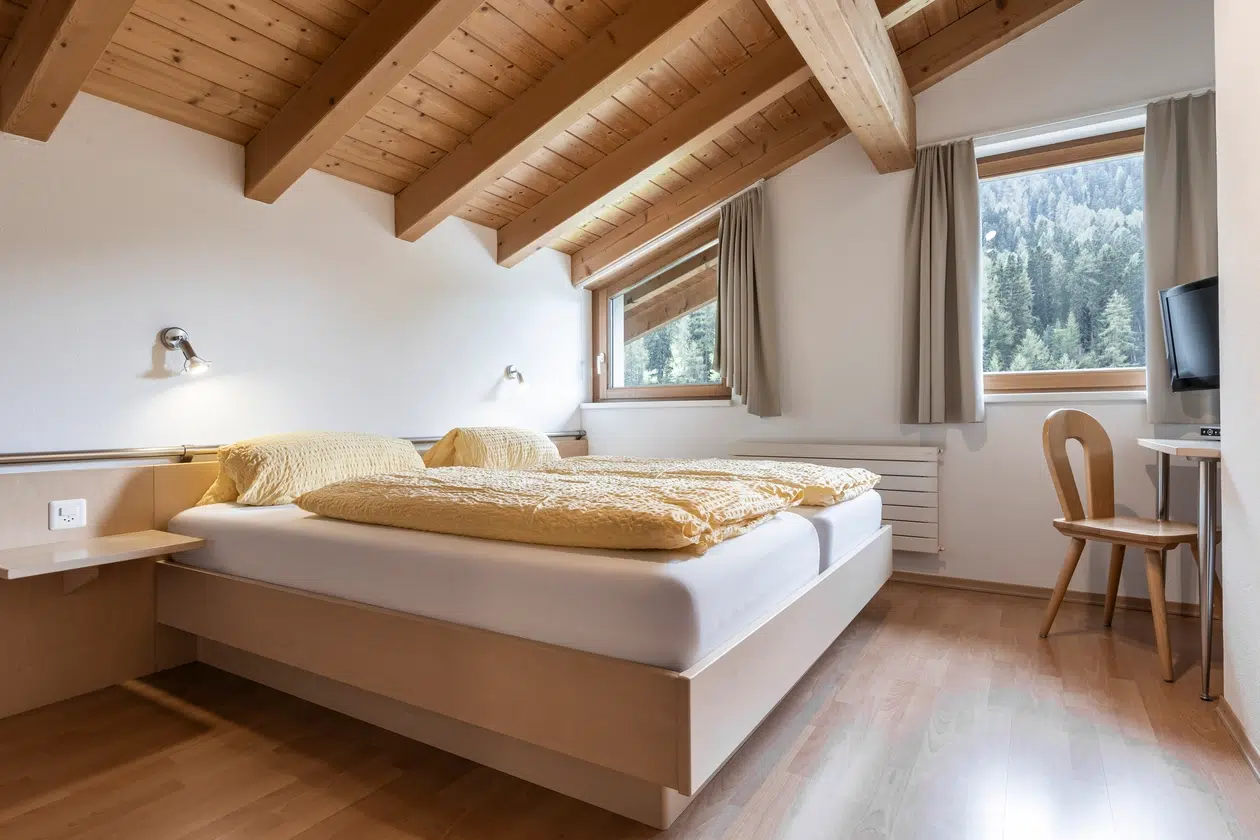 Gemütliches Schlafzimmer mit Holzdecke, Doppelbett, TV und Waldblick in der Ferienwohnung Samnaun.