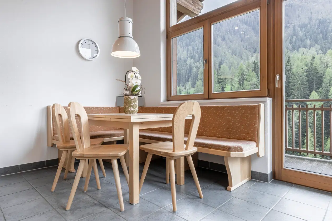 Hölzerne Essecke in der Ferienwohnung Samnaun, mit Tisch und Bank am großen Panoramafenster.