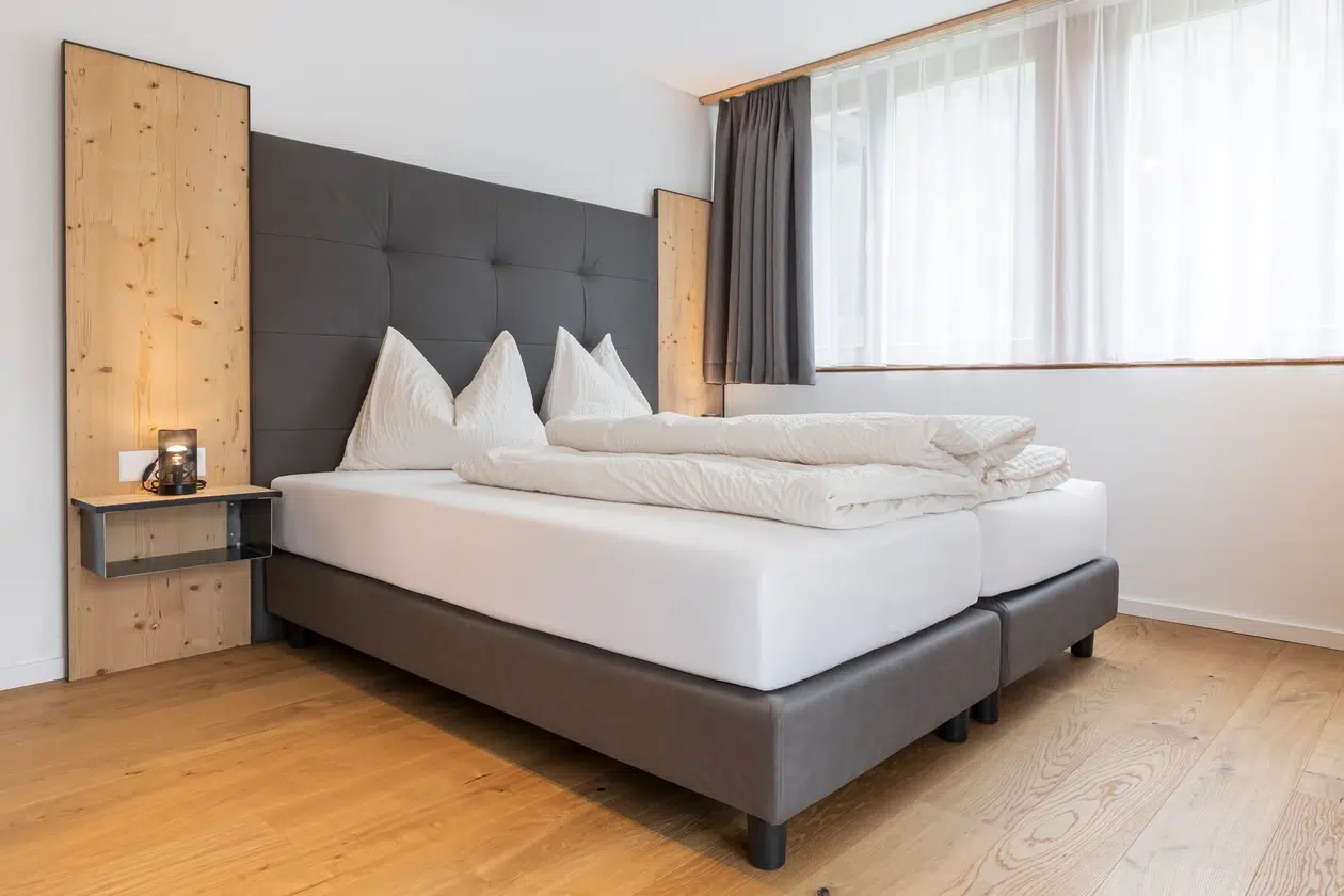 Modernes Schlafzimmer mit Doppelbett, Holzboden und großem Fenster mit Gardinen.