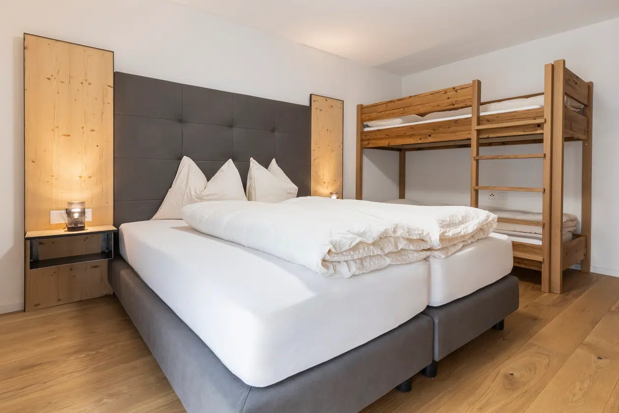 Modernes Schlafzimmer im ferienhaus samnaun mit Doppelbett und Etagenbetten aus Holz auf Hartholzboden.
