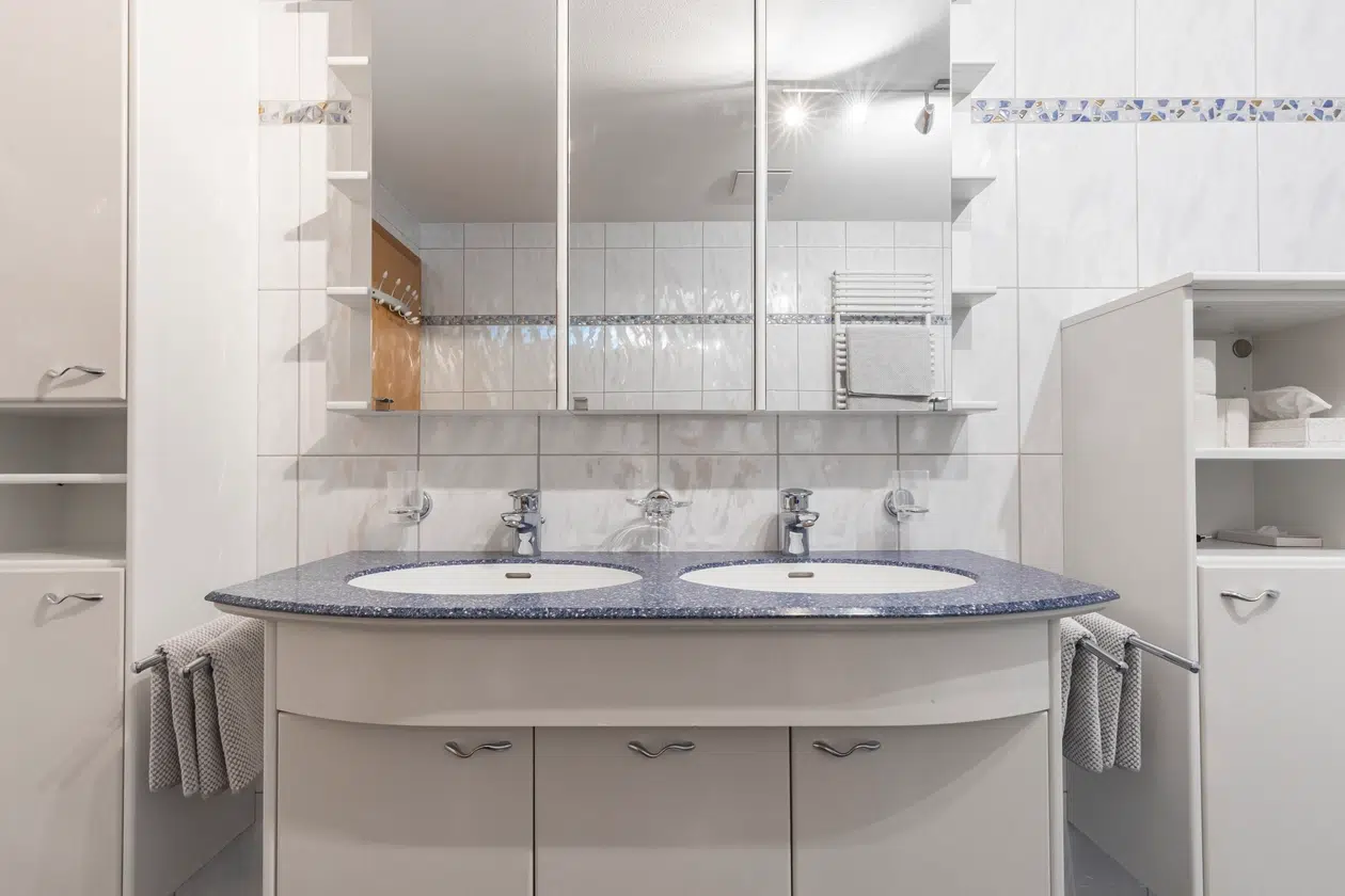 Modernes Badezimmer mit Doppelwaschbecken, großem Spiegel und weißen Schränken.