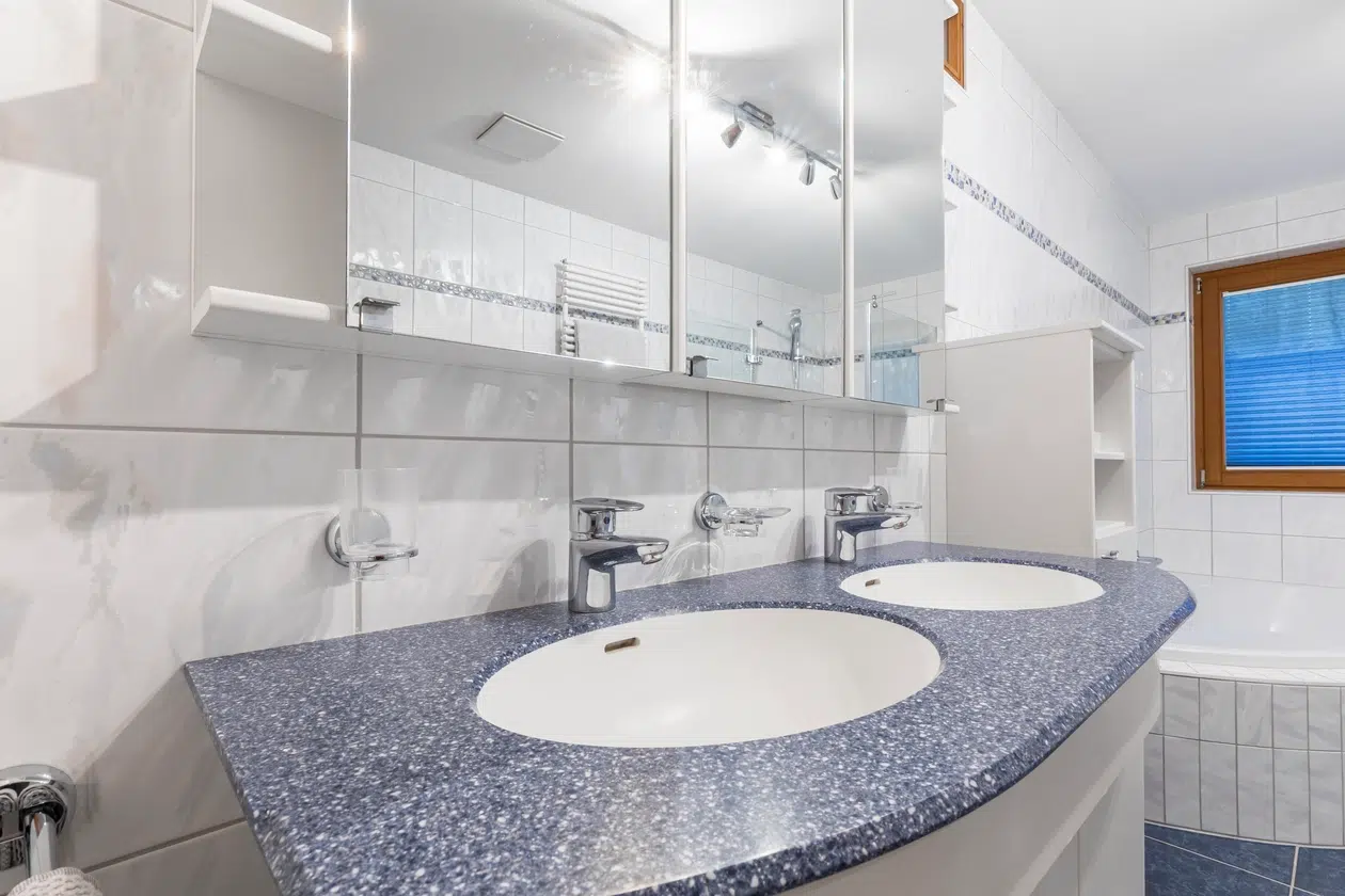 Doppelter Waschtisch mit blauer Arbeitsplatte und weiß gefliesten Wänden.