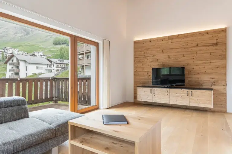 Modernes Wohnzimmer in einem Ferienhaus Samnaun mit grauem Sofa, TV, Holzakzenten und Bergblick.