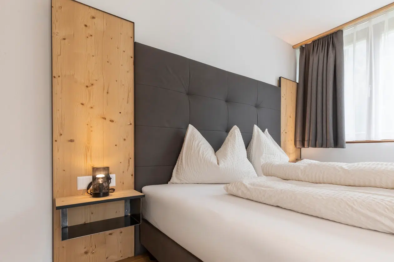 Modernes Schlafzimmer mit ordentlich gemachtem Bett, Holzkopfteil und einer Lampe auf dem Nachttisch.