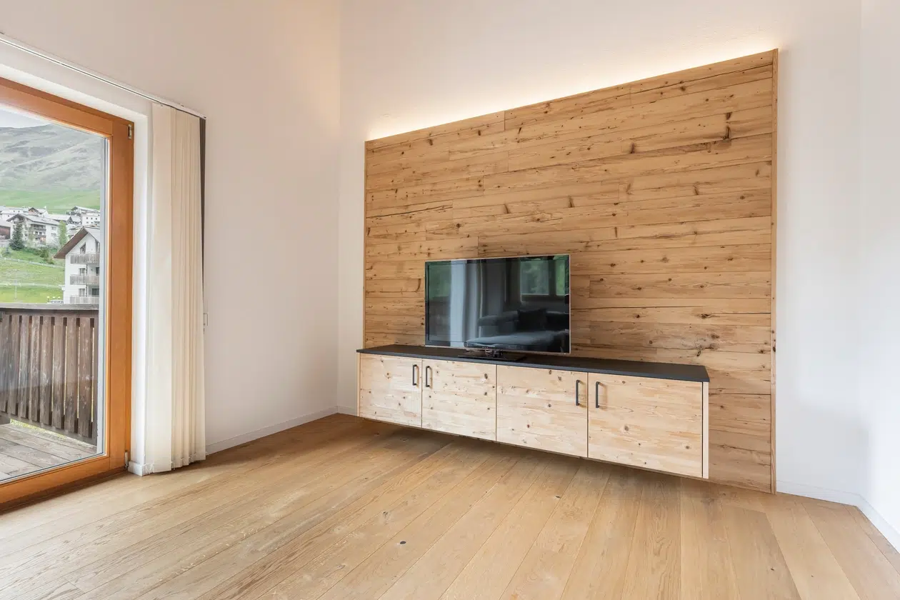 TV auf einem Holzschrank vor einer Akzentwand aus Holz in einem hellen, modernen Wohnzimmer mit Balkon.