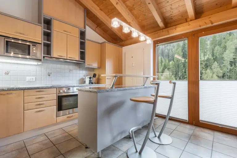 Moderne Küche im ferienhaus Samnaun mit Holzschränken, Insel und Waldblickfenster.