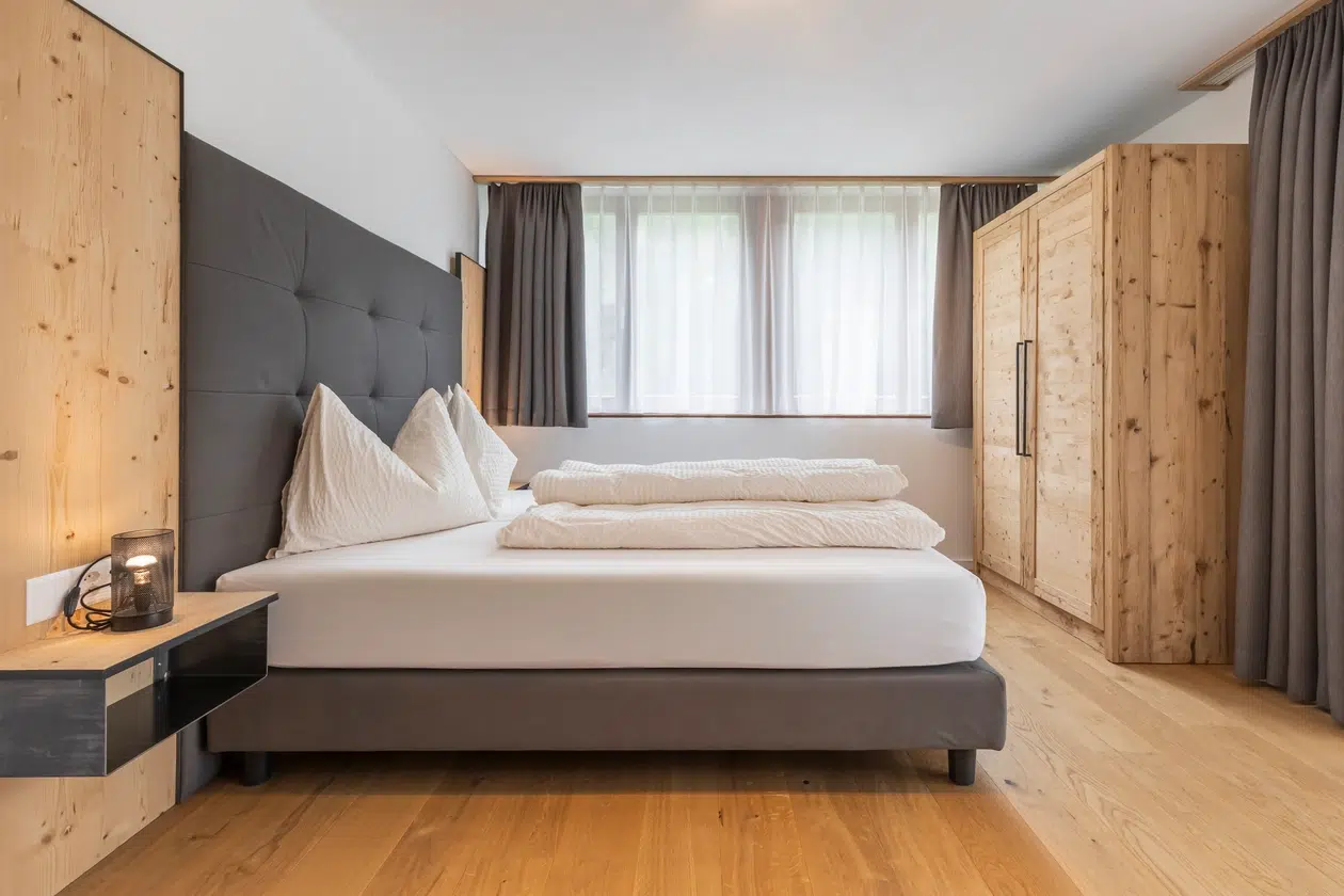 Modernes Schlafzimmer mit einem Doppelbett, Holzmöbeln und einem großen Fenster mit Vorhängen.
