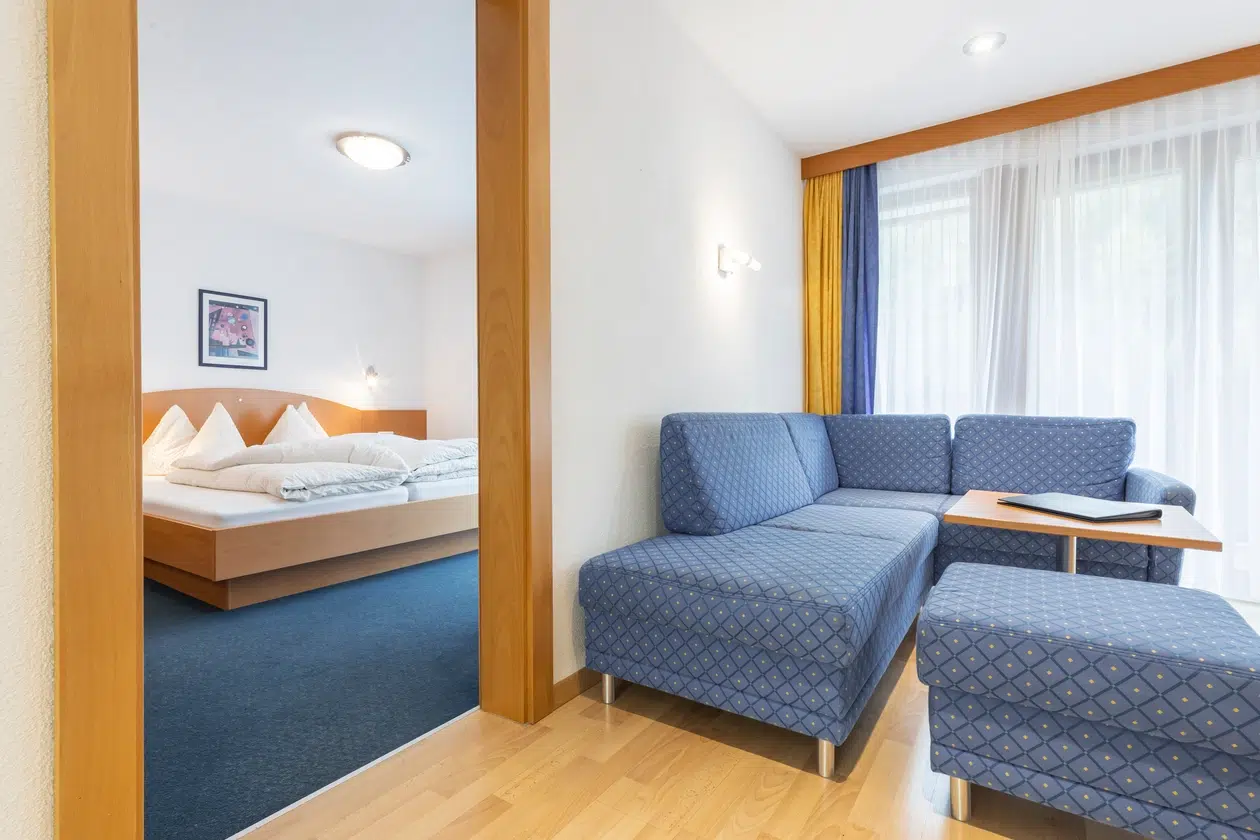 Ein modernes Apartment Samnaun mit einem blauen Sofa und einem Bett in einem Nebenraum.