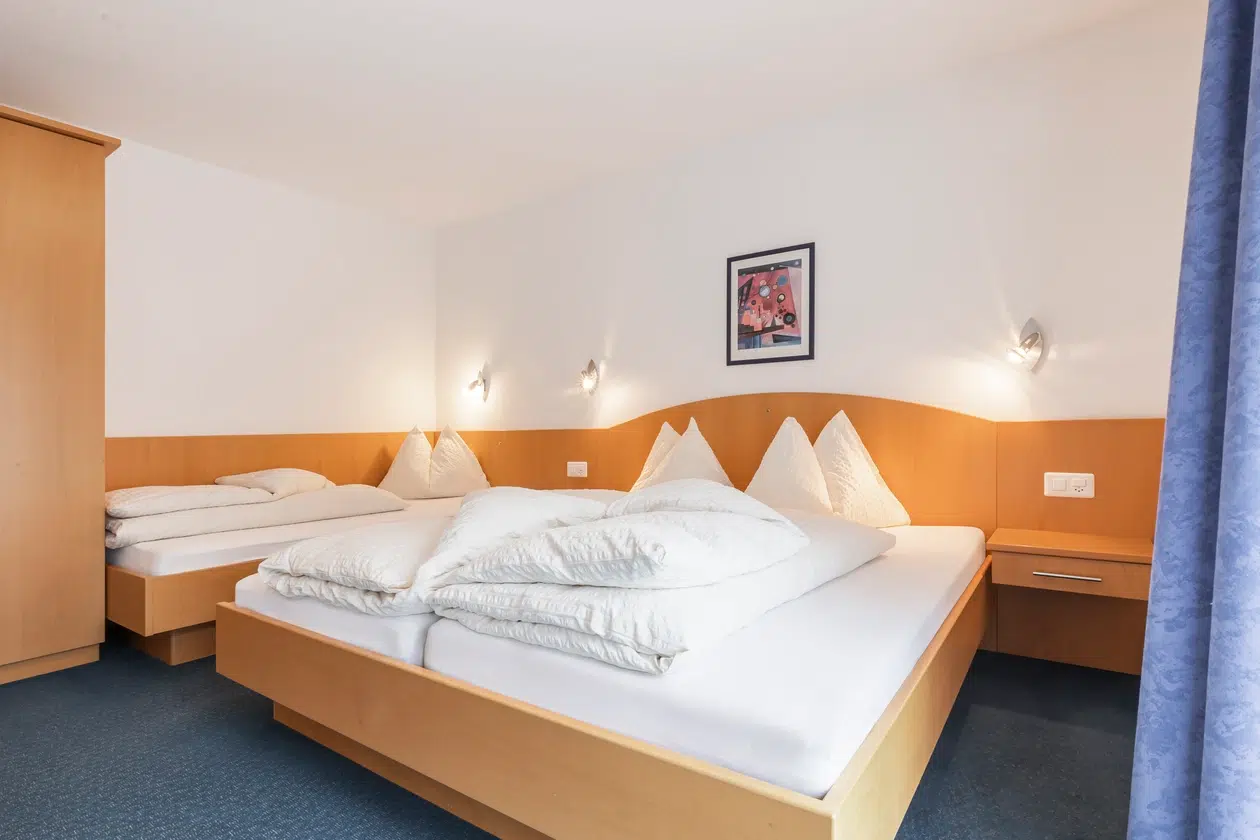 Ein ordentliches Zimmer im Apartment Samnaun mit zwei Betten, weißem Bettzeug, Holzmöbeln und einem Wandgemälde.